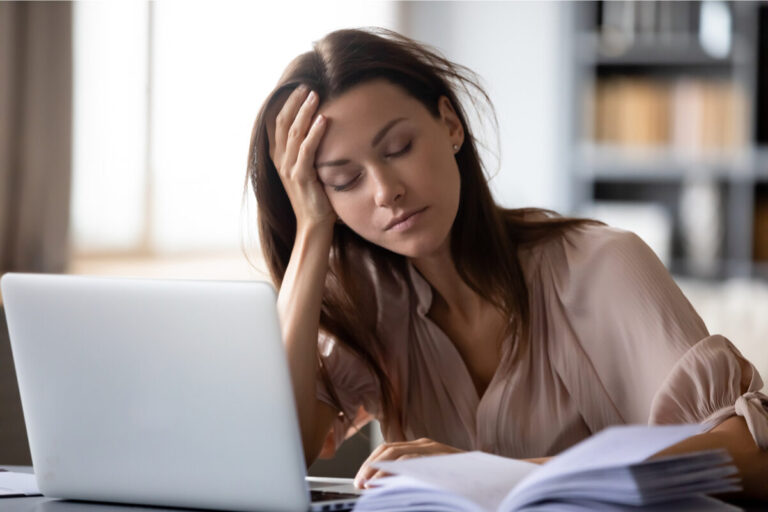 ragazza mora con capelli lunghi e camicia beige alla scrivania stanca con occhi chiusi. lavora al computer e studia un libro