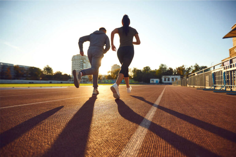 ragazzo e ragazza di spalle corrono al tramonto su una pista di atletica