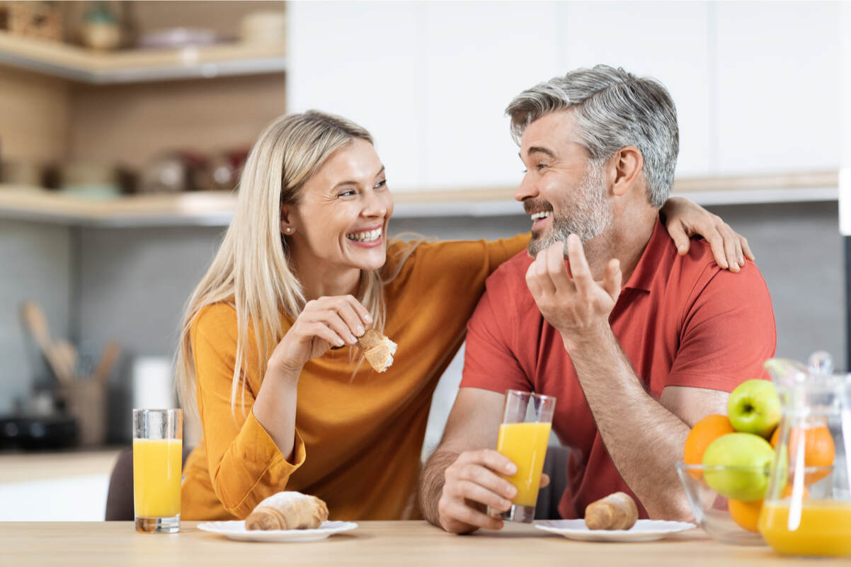 coppia felice che fa colazione in casa con cornetto e spremuta di arancia